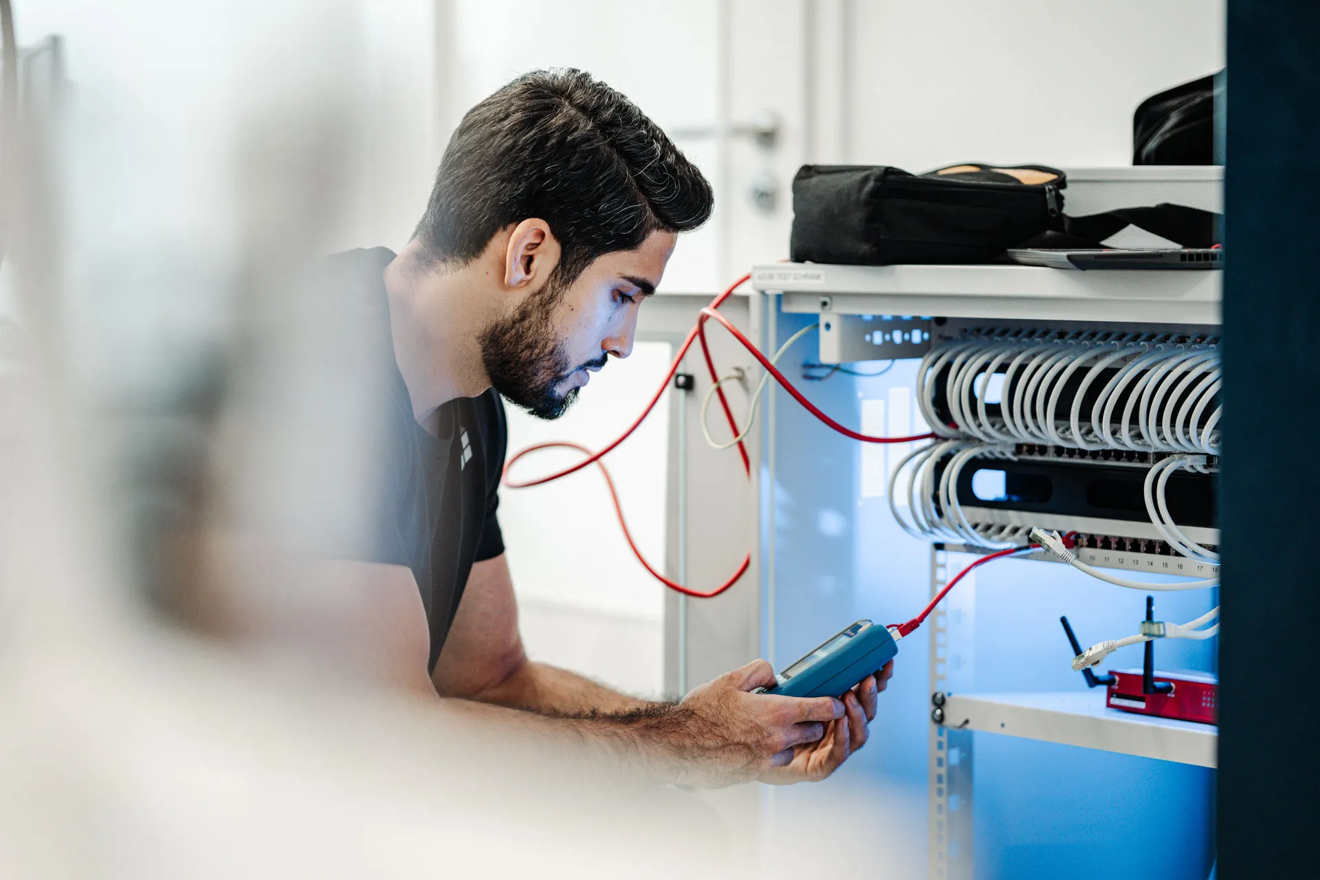 Techniker prüft ein Patchpanel im Serverschrank mit einem Kabeltester